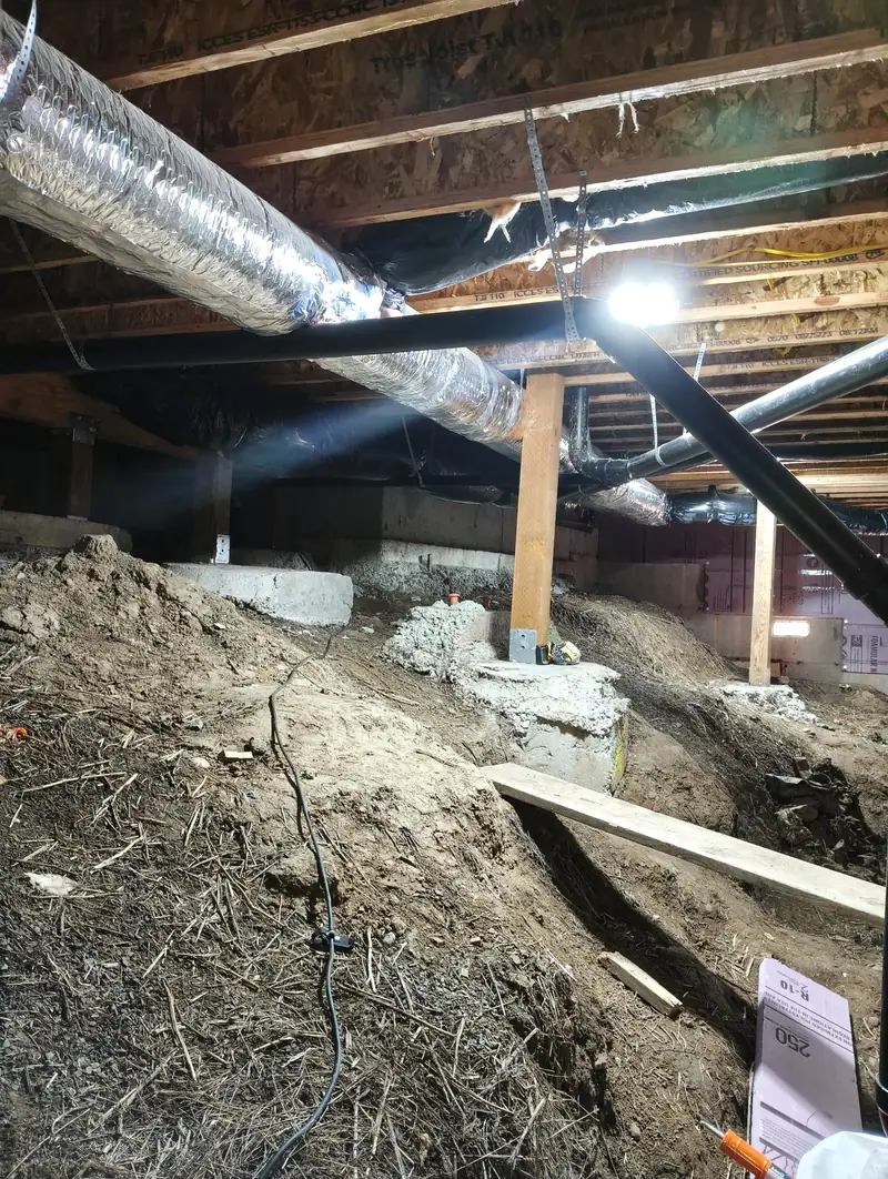 Crawl space with mounded bare soil under ducts and plumbing before encapsulation