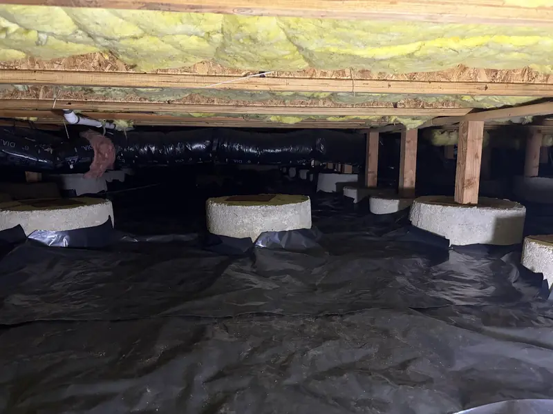 Concrete piers and wood posts above a black crawl space barrier